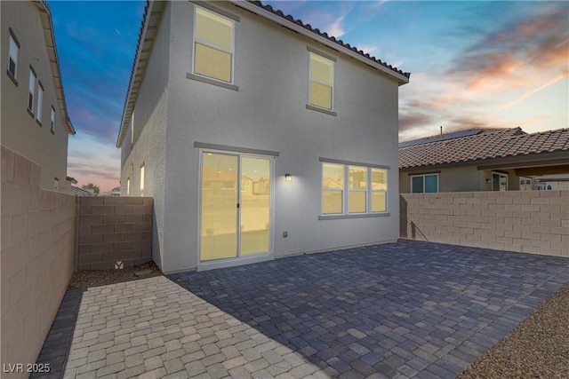 back of house at dusk featuring a patio area, a fenced backyard, a tiled roof, and stucco siding