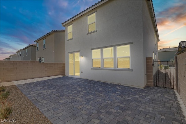 back of property at dusk featuring a patio area, fence, a gate, and stucco siding