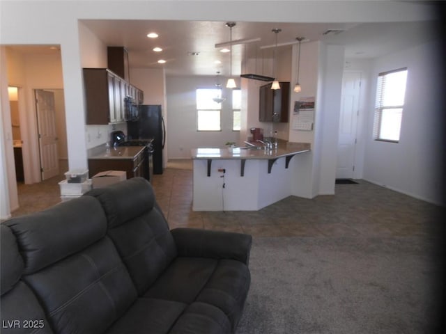 kitchen with a breakfast bar, open floor plan, light tile patterned flooring, black microwave, and a peninsula