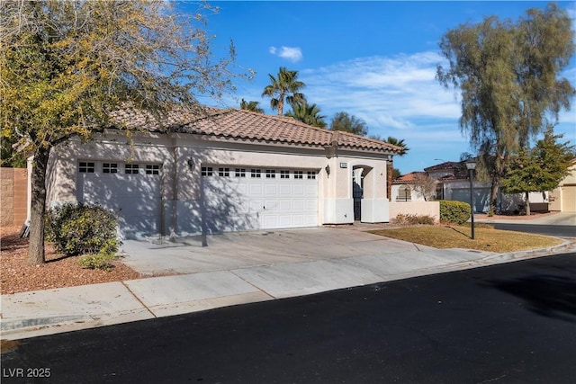 mediterranean / spanish-style home featuring a garage, a tiled roof, concrete driveway, and stucco siding