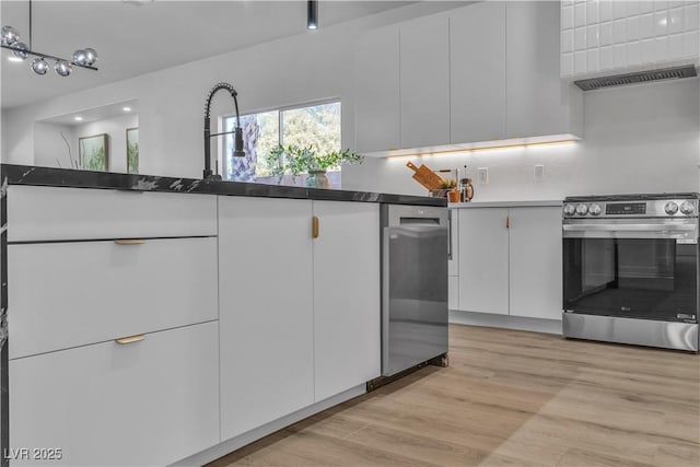 kitchen featuring white cabinetry, light wood finished floors, stainless steel range, dark countertops, and tasteful backsplash