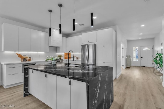 kitchen featuring white cabinets, an island with sink, light wood-style flooring, freestanding refrigerator, and pendant lighting