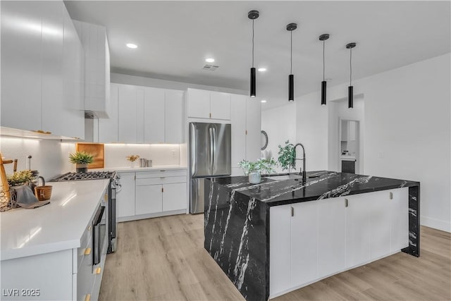 kitchen featuring stainless steel appliances, a sink, white cabinets, an island with sink, and decorative light fixtures