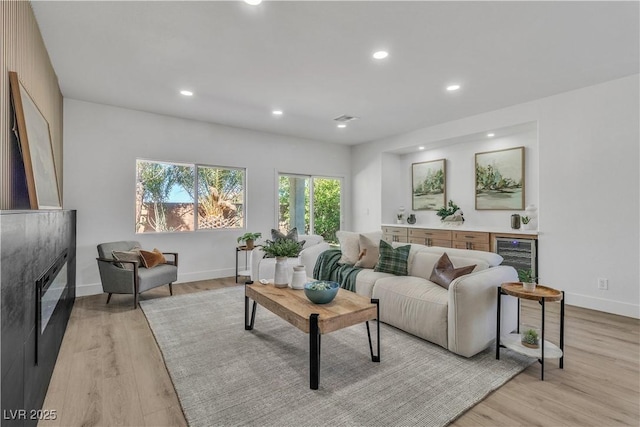 living area featuring light wood-type flooring, beverage cooler, recessed lighting, and a glass covered fireplace