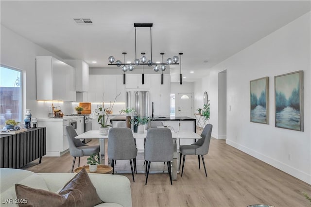 dining area featuring light wood-type flooring, visible vents, a notable chandelier, and baseboards