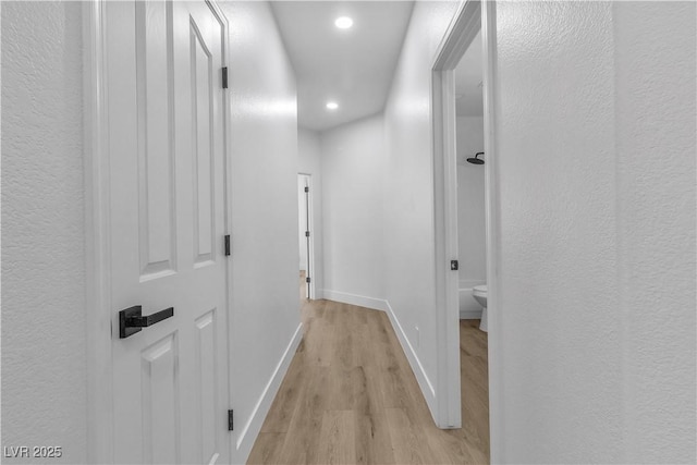 hallway with a textured wall, light wood finished floors, recessed lighting, and baseboards