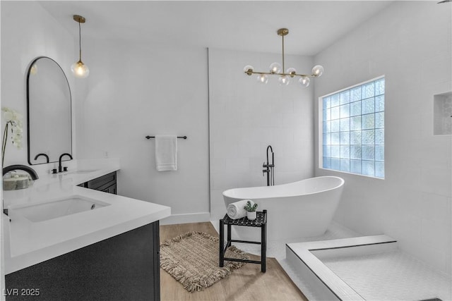 full bathroom featuring double vanity, a freestanding tub, a chandelier, and a sink