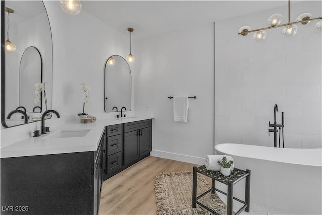 bathroom with wood finished floors, a sink, baseboards, a soaking tub, and double vanity