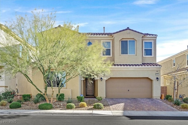 mediterranean / spanish house with an attached garage, a tiled roof, decorative driveway, and stucco siding