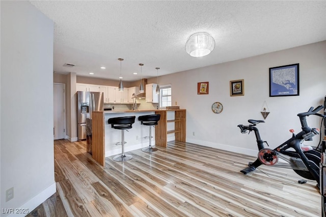 kitchen featuring a peninsula, hanging light fixtures, wall chimney range hood, light countertops, and stainless steel fridge