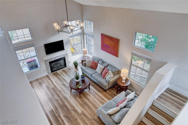 living area with baseboards, a chandelier, a glass covered fireplace, wood finished floors, and high vaulted ceiling