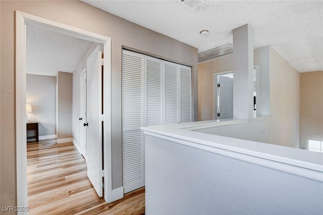 corridor featuring light wood finished floors, baseboards, visible vents, and a textured ceiling