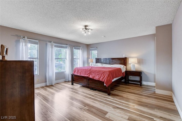 bedroom featuring light wood-type flooring, baseboards, and a textured ceiling