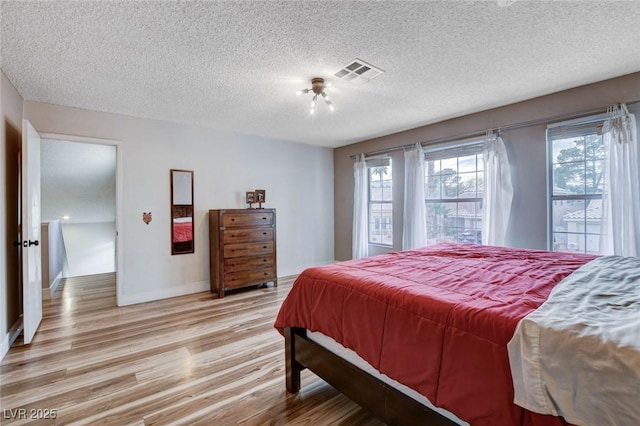 bedroom featuring baseboards, light wood-style flooring, visible vents, and a textured ceiling