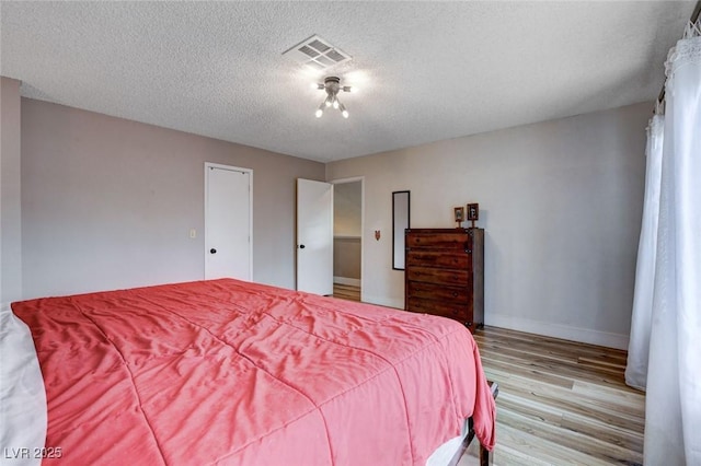 bedroom with a textured ceiling, baseboards, visible vents, and light wood-style floors