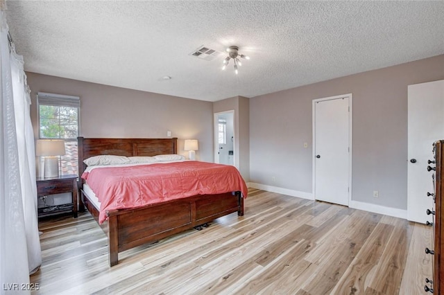 bedroom featuring light wood-type flooring, baseboards, visible vents, and a textured ceiling