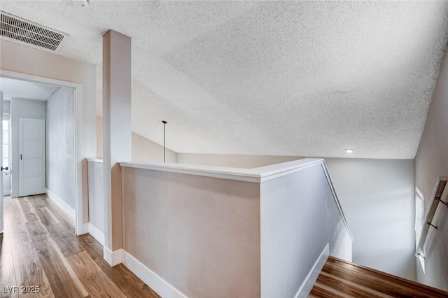 corridor with light wood-style flooring, visible vents, baseboards, and an upstairs landing