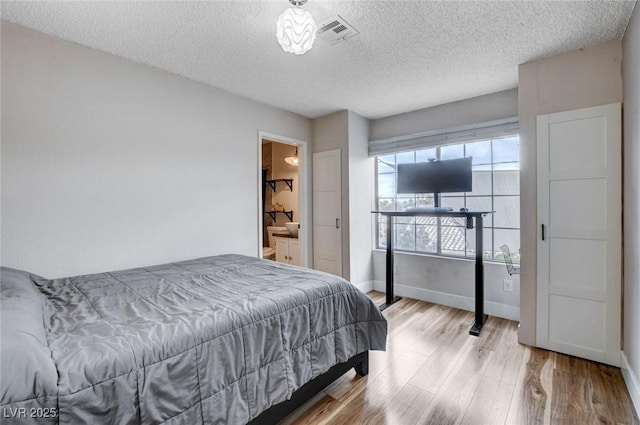 bedroom featuring light wood finished floors, baseboards, visible vents, and a textured ceiling