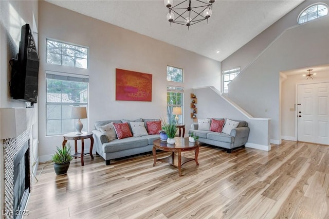 living room with high vaulted ceiling, baseboards, light wood-style floors, stairs, and an inviting chandelier