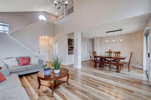 living room featuring baseboards, light wood-style flooring, visible vents, and a notable chandelier