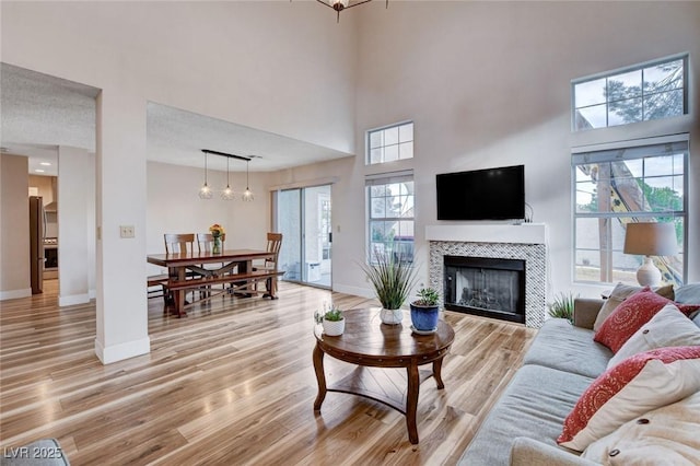 living area with a towering ceiling, light wood-style floors, baseboards, and a tiled fireplace