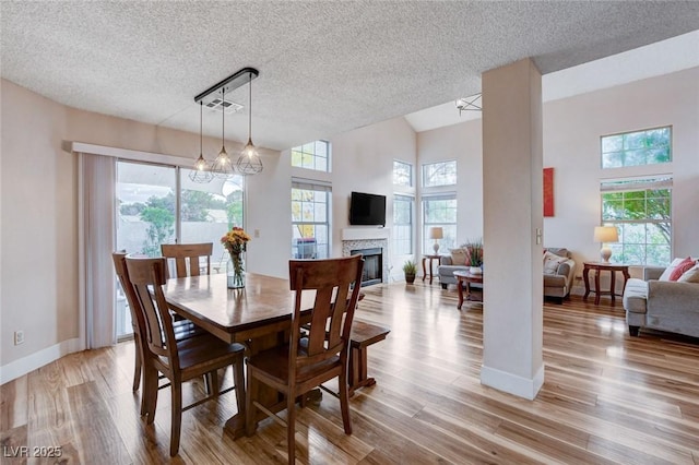 dining room with light wood-style floors, plenty of natural light, a fireplace, and baseboards