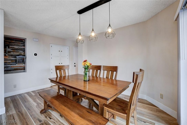 dining area featuring a textured ceiling, light wood finished floors, and baseboards