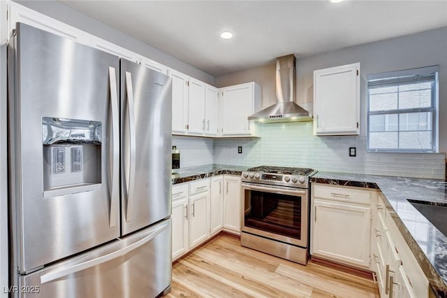 kitchen with appliances with stainless steel finishes, backsplash, wall chimney range hood, and white cabinetry