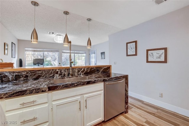 kitchen featuring dark stone countertops, pendant lighting, white cabinets, and stainless steel dishwasher