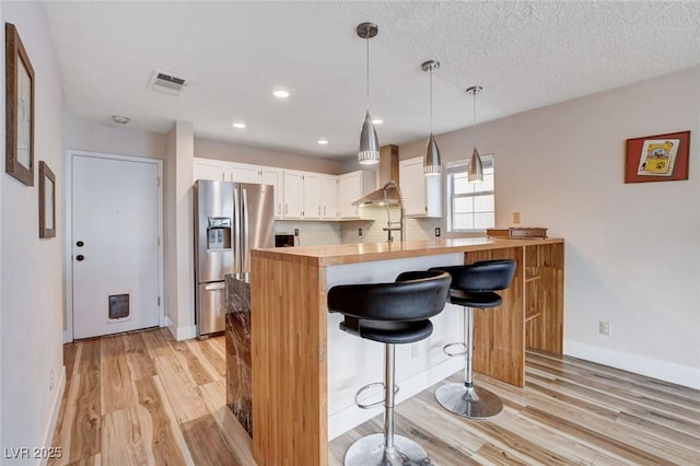 kitchen featuring stainless steel refrigerator with ice dispenser, visible vents, hanging light fixtures, white cabinetry, and a peninsula