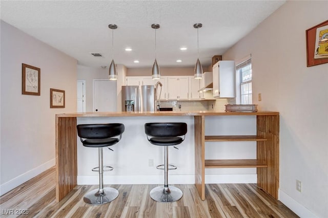 kitchen featuring a breakfast bar, white cabinetry, stainless steel refrigerator with ice dispenser, and decorative light fixtures