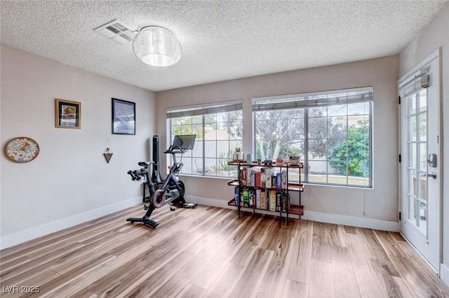 workout area with visible vents, a textured ceiling, light wood-style flooring, and baseboards