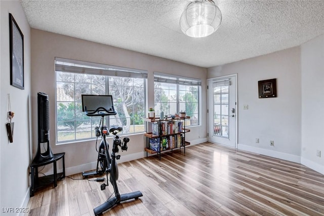 exercise area with a healthy amount of sunlight, a textured ceiling, baseboards, and wood finished floors