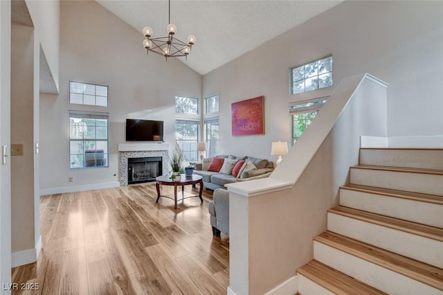 living area with light wood finished floors, baseboards, stairway, a fireplace, and high vaulted ceiling