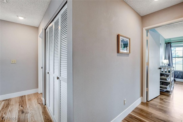 hall with a textured ceiling, light wood-type flooring, and baseboards