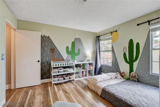 bedroom featuring a textured ceiling, multiple windows, wood finished floors, and visible vents