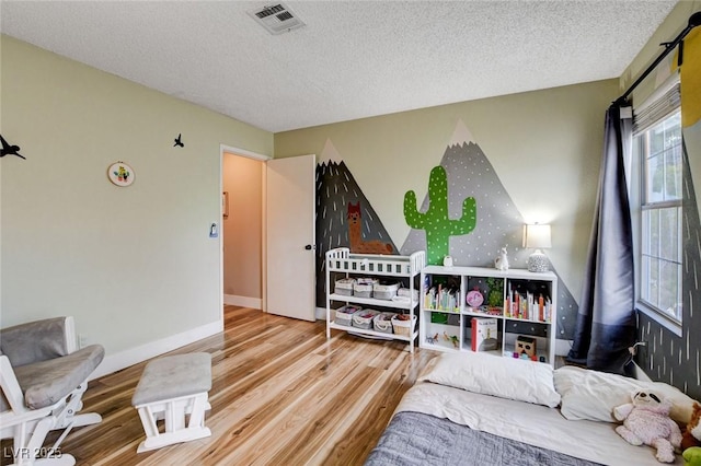 bedroom featuring visible vents, a textured ceiling, baseboards, and wood finished floors