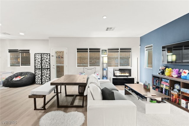 living area with visible vents, wood finished floors, and a glass covered fireplace