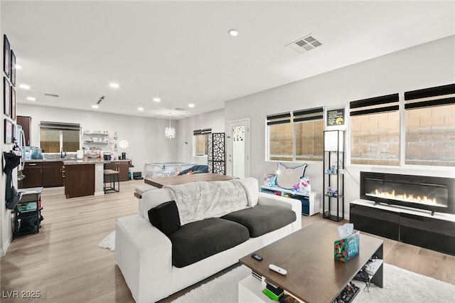 living area featuring light wood-style flooring, a glass covered fireplace, visible vents, and recessed lighting