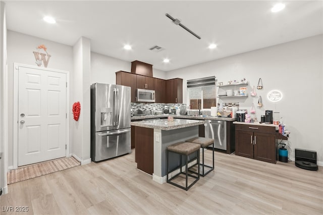 kitchen with dark brown cabinetry, visible vents, a kitchen island, a breakfast bar area, and stainless steel appliances