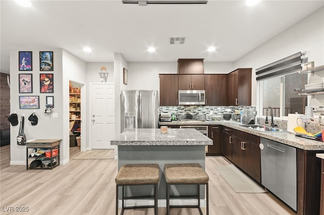 kitchen with stainless steel appliances, a sink, visible vents, dark brown cabinets, and a center island