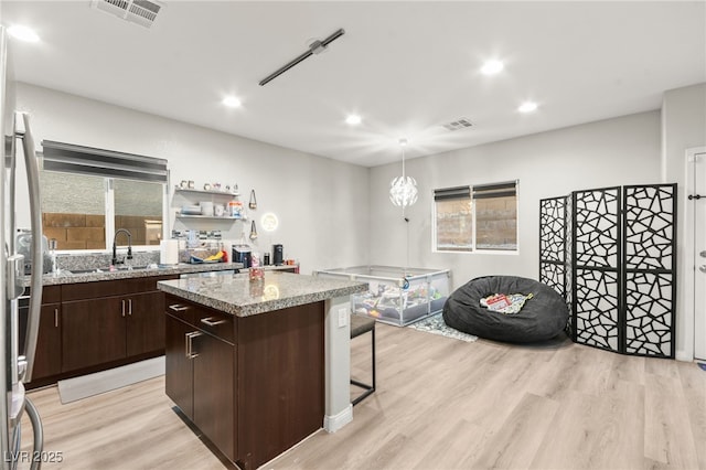 kitchen featuring dark brown cabinetry, visible vents, a center island, open shelves, and a sink