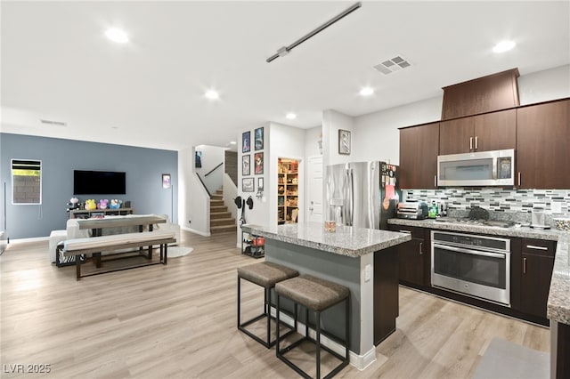 kitchen featuring a center island, stainless steel appliances, visible vents, open floor plan, and dark brown cabinets