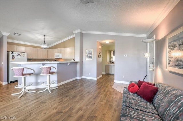 kitchen with a peninsula, white appliances, wood finished floors, visible vents, and vaulted ceiling