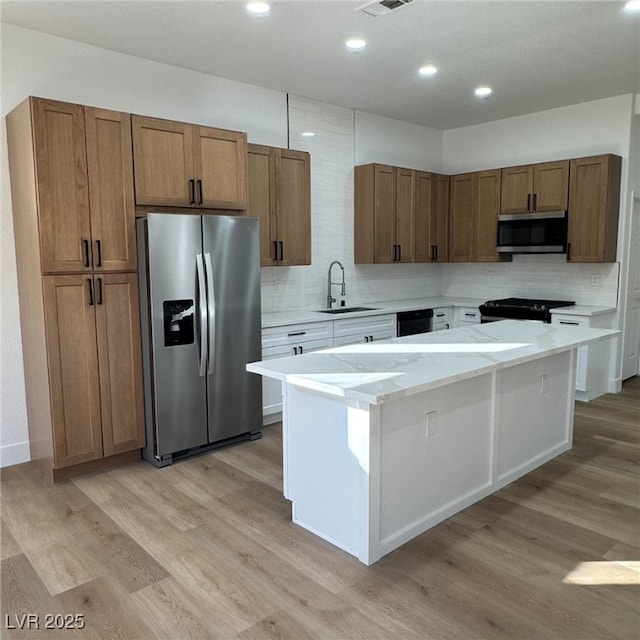 kitchen with black appliances, a kitchen island, brown cabinets, and a sink