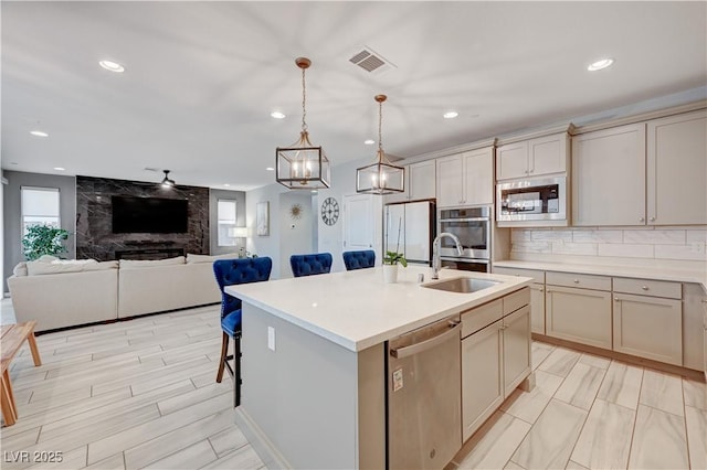 kitchen with a sink, light countertops, appliances with stainless steel finishes, a center island with sink, and pendant lighting