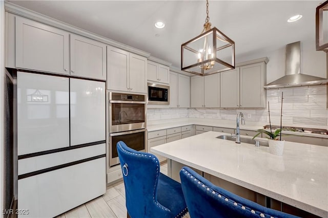 kitchen with a kitchen breakfast bar, decorative light fixtures, gray cabinets, stainless steel appliances, and wall chimney range hood