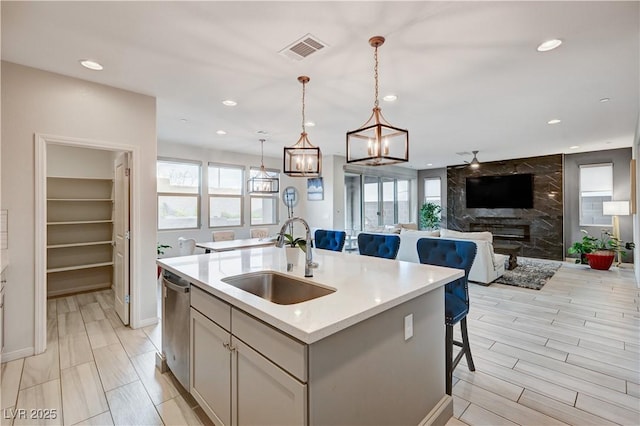 kitchen featuring hanging light fixtures, stainless steel dishwasher, open floor plan, a kitchen island with sink, and a sink