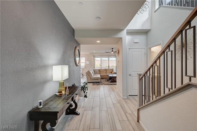 entryway featuring baseboards, a ceiling fan, a textured wall, stairs, and wood finish floors