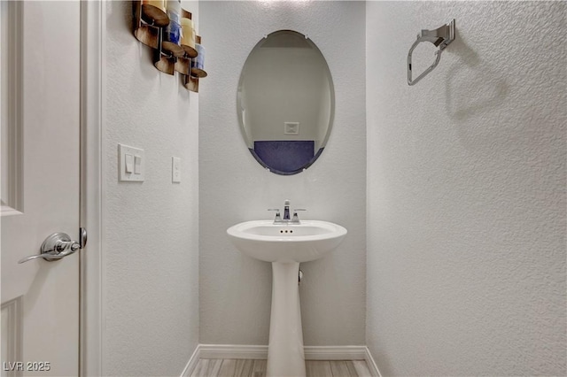 bathroom with baseboards, wood finished floors, and a textured wall